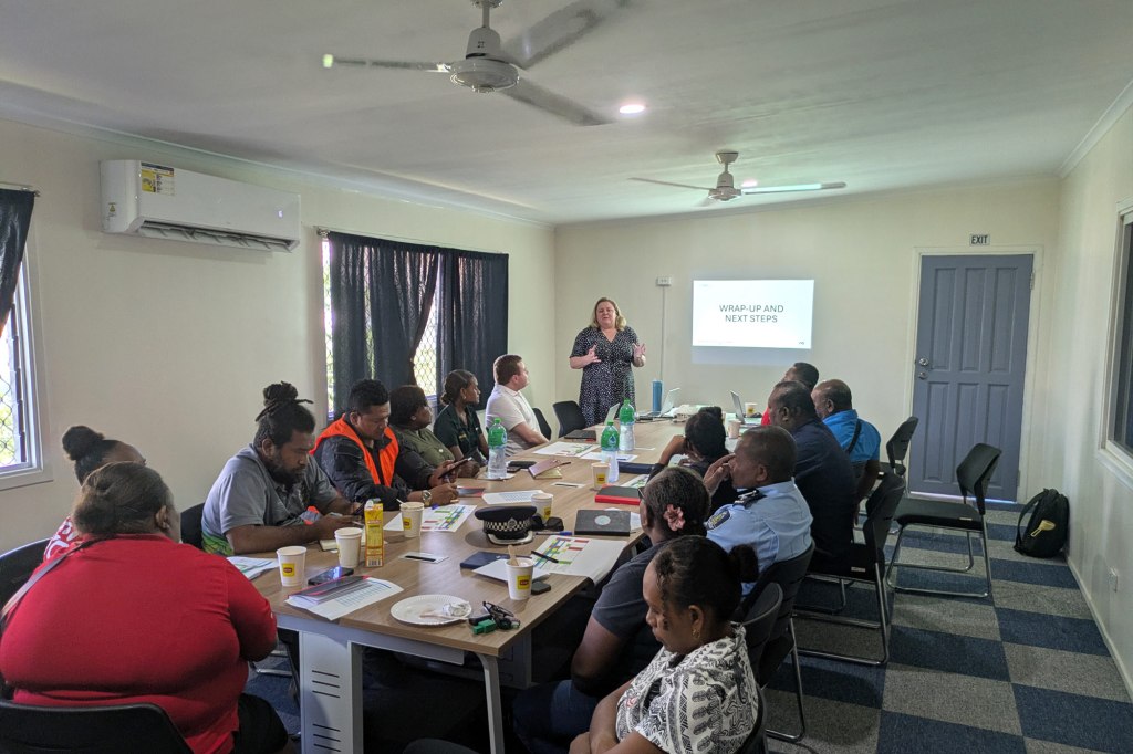 Road safety workshop session in the Solomon Islands with participants seated around a table during a presentation led by a facilitator
