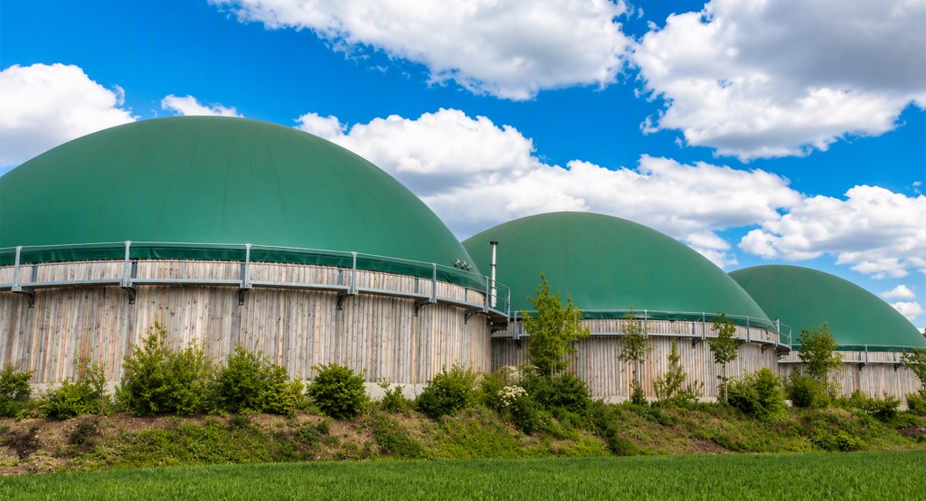 iogas and biomethane plant with large green anaerobic digestion tanks under a blue sky.