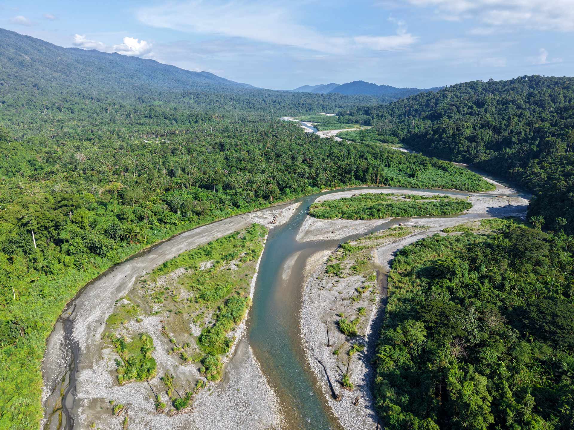 Aerial view of a winding river flowing through a lush tropical forest valley surrounded by green mountains.