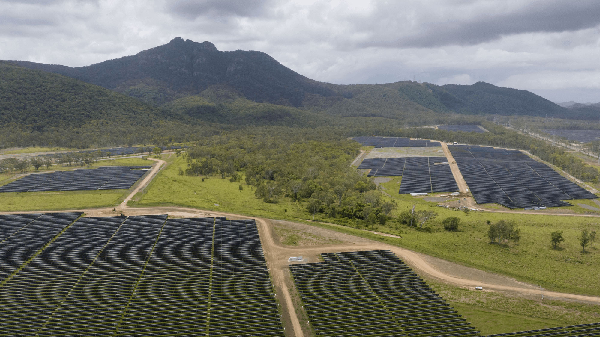 Aerial view of a large solar farm with rows of dark solar panels stretching across a green landscape.