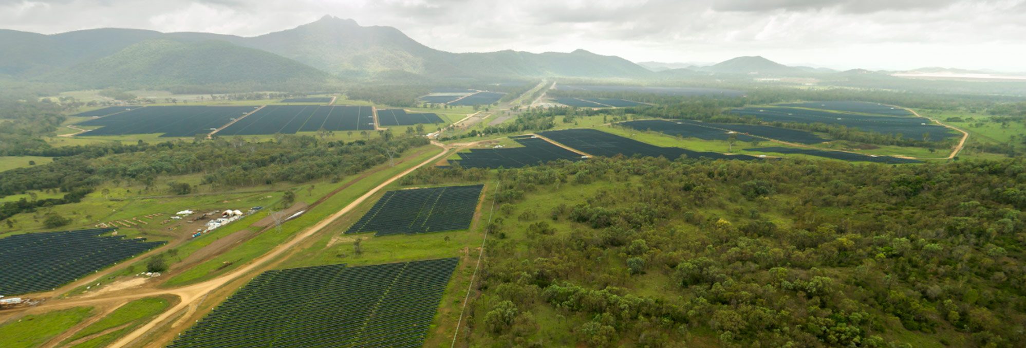 Aerial view of a large solar farm with rows of dark solar panels stretching across a green landscape.