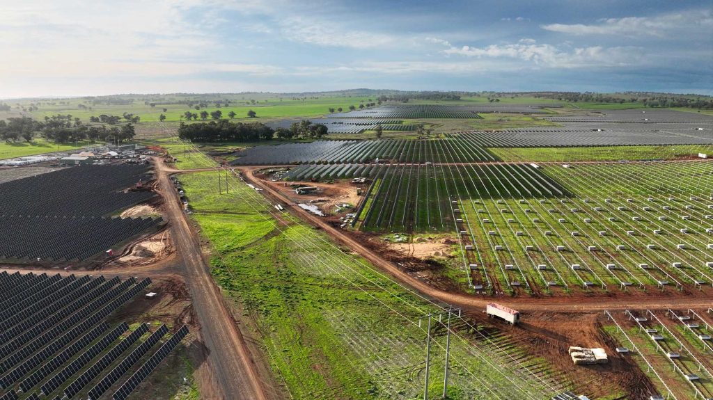 Aerial view of the Maryvale Solar and Energy Storage Project, showing extensive rows of solar panels and battery storage infrastructure under construction across rural farmland, with access roads, power lines, and a dramatic cloudy sky.