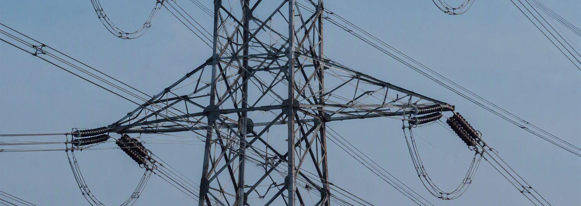 Close-up view of a high-voltage transmission tower and power lines against a blue sky.