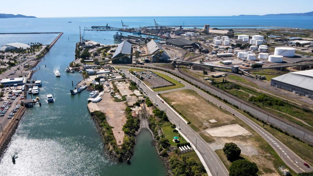 A panoramic aerial view of a large coastal industrial port and shipping terminal situated along a sheltered blue harbor.