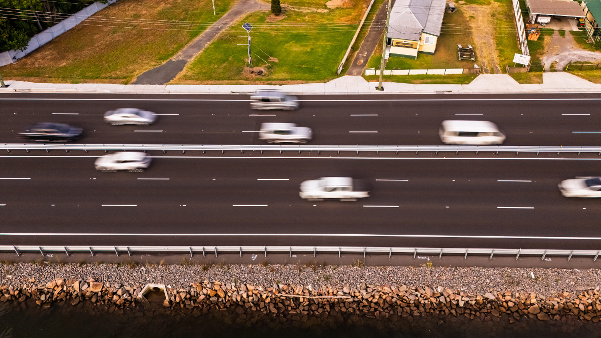 Aerial view of a multi-lane highway bridge crossing a winding river and wetlands in Hexham, with cars blurred in motion.