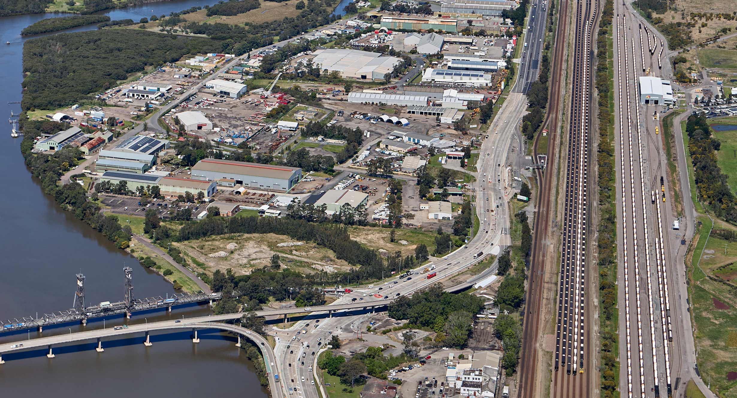 Aerial view of Hexham, showing a widened highway running alongside wetlands and a waterway, with vehicles traveling under overcast skies.