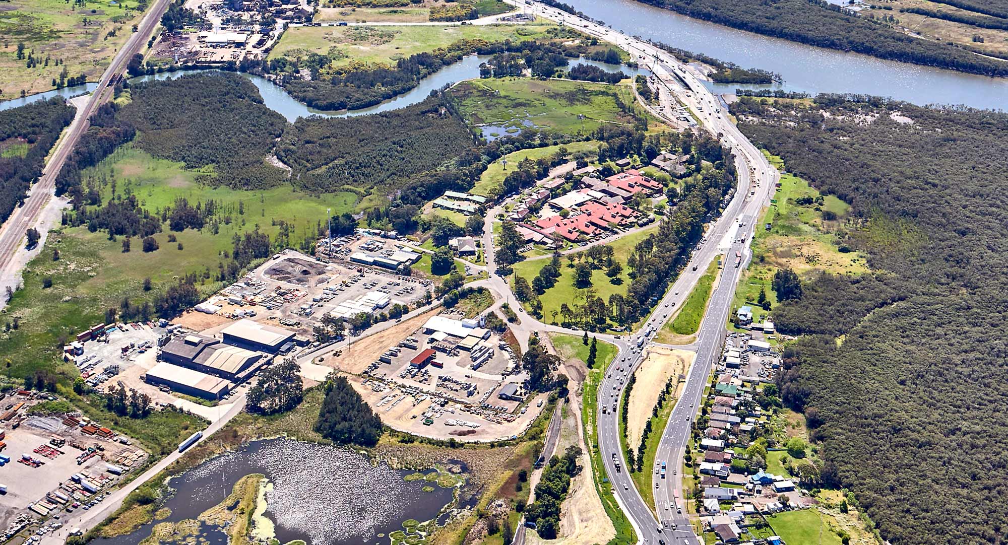 Aerial view of Hexham, showing a widened highway running alongside wetlands and a waterway, with vehicles traveling under overcast skies.