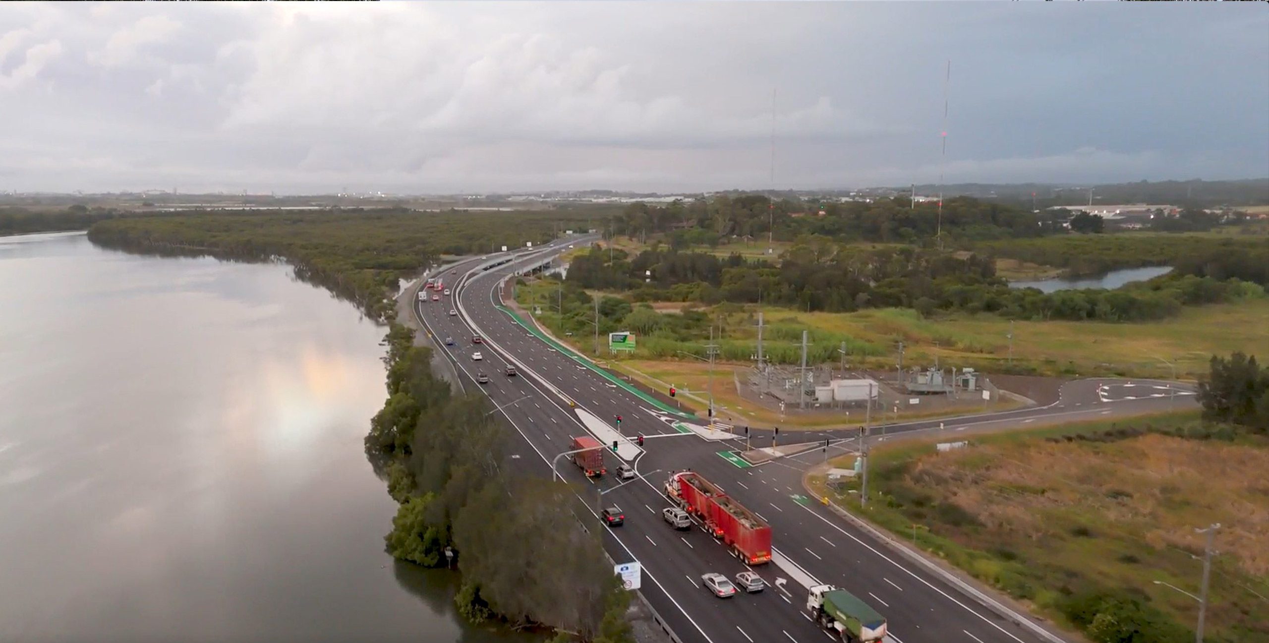 Aerial view of Hexham, showing a widened highway running alongside wetlands and a waterway, with vehicles traveling under overcast skies.