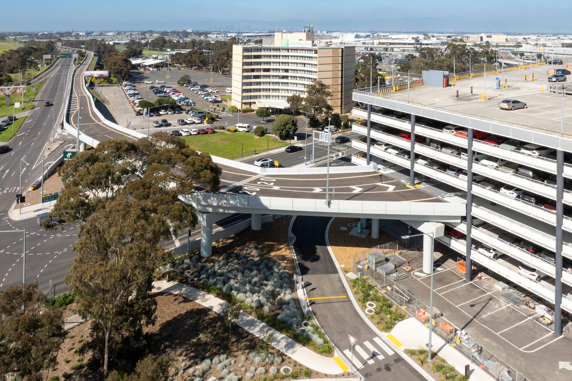 Elevated roadway and multi-storey car park along Melbourne Airport’s Naarm Way, viewed from above with surrounding transport and airport facilities.