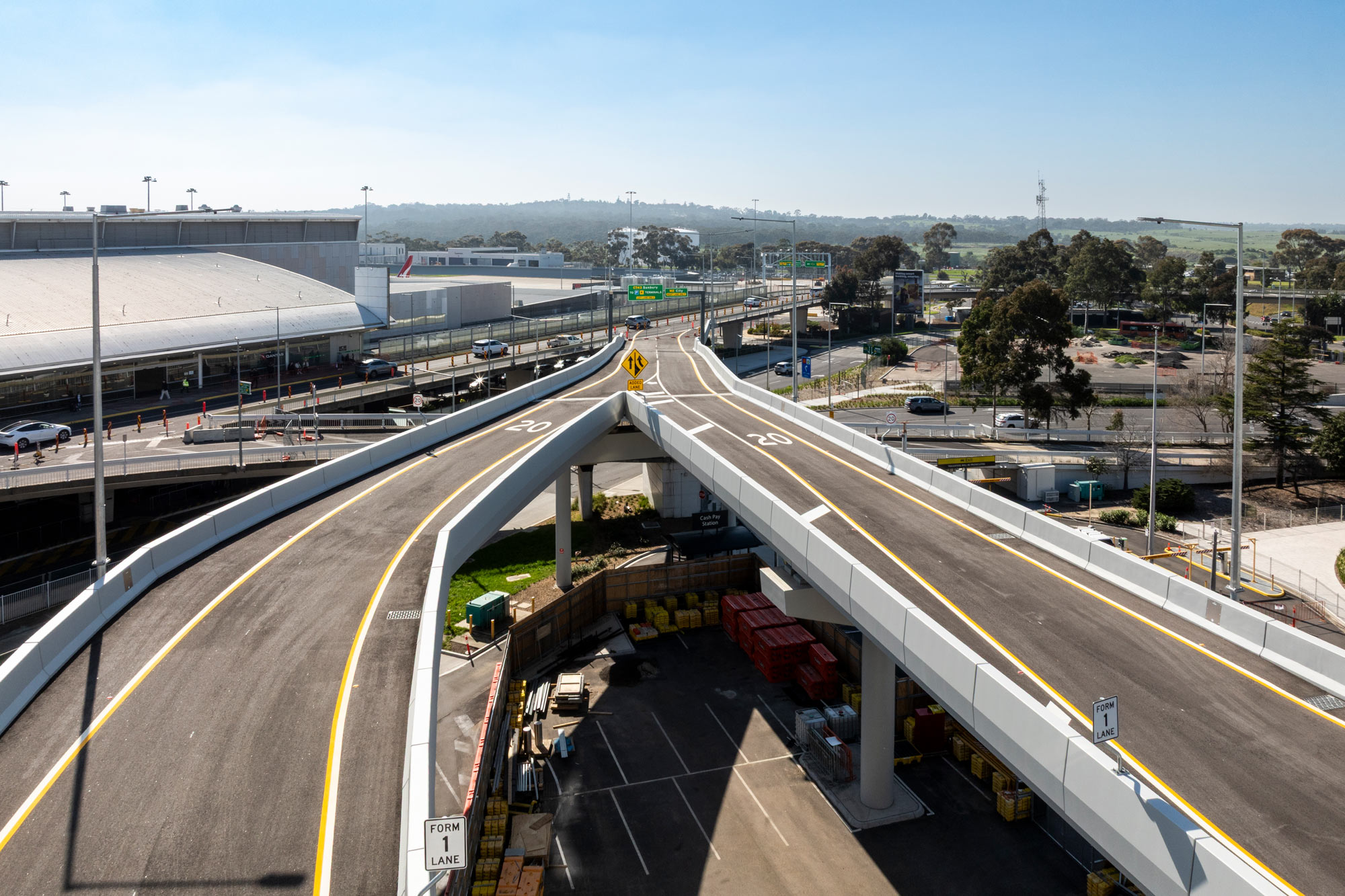High-angle view of Melbourne Airport’s Naarm Way featuring twin elevated roadway ramps and terminal access roads.