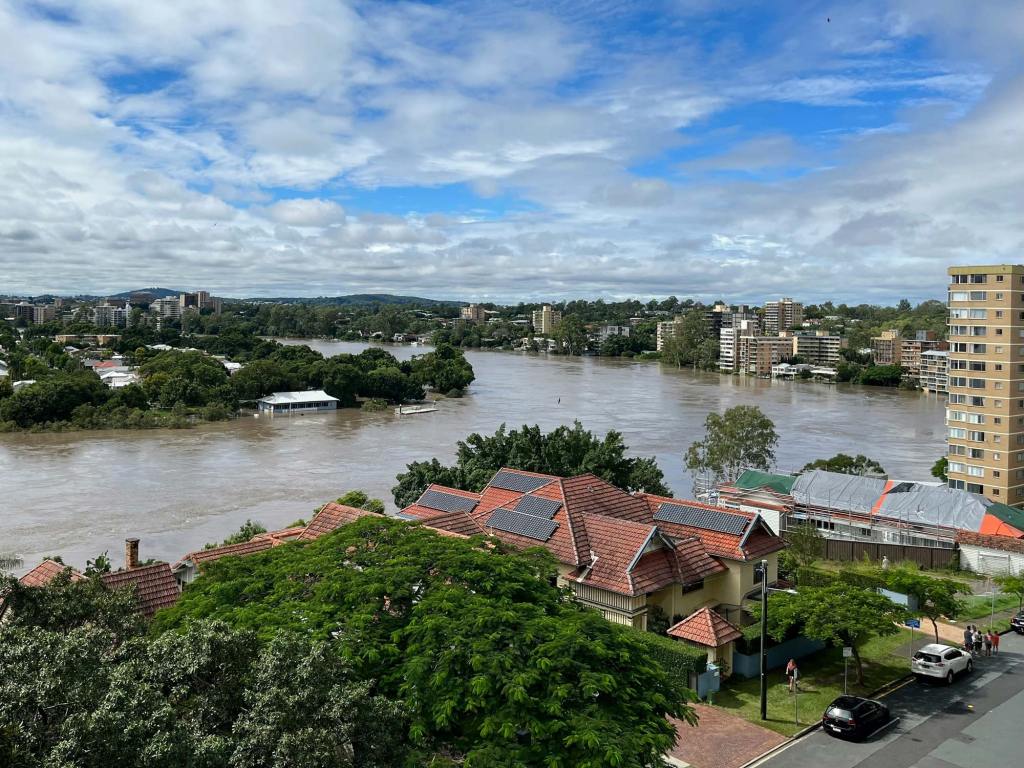 Brisbane River with elevated water levels alongside nearby residential and apartment buildings.