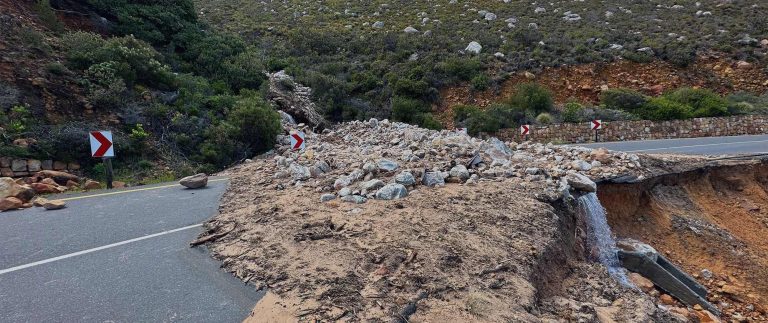 Road damaged by landslide and erosion, with rocks and debris blocking part of a mountain roadway.