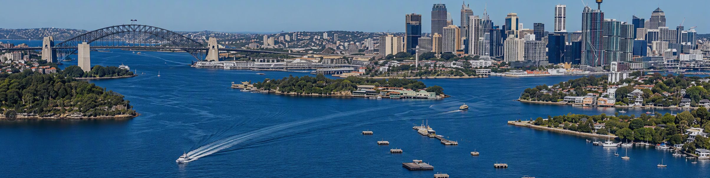 Sydney Harbour aerial view with Sydney Harbour Bridge, city skyline, and blue harbor waters.